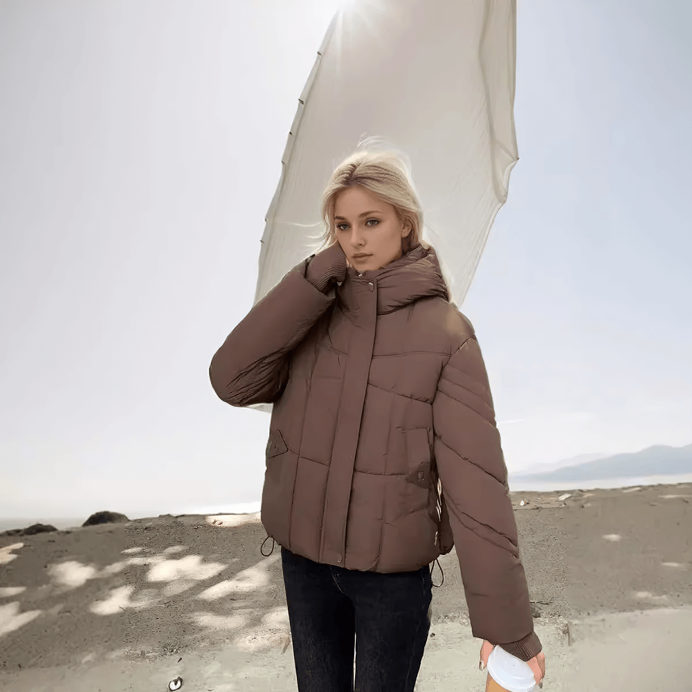 Woman wearing chic beige quilted jacket with hood and ribbed cuffs, standing outdoors, showcasing stylish winter outerwear