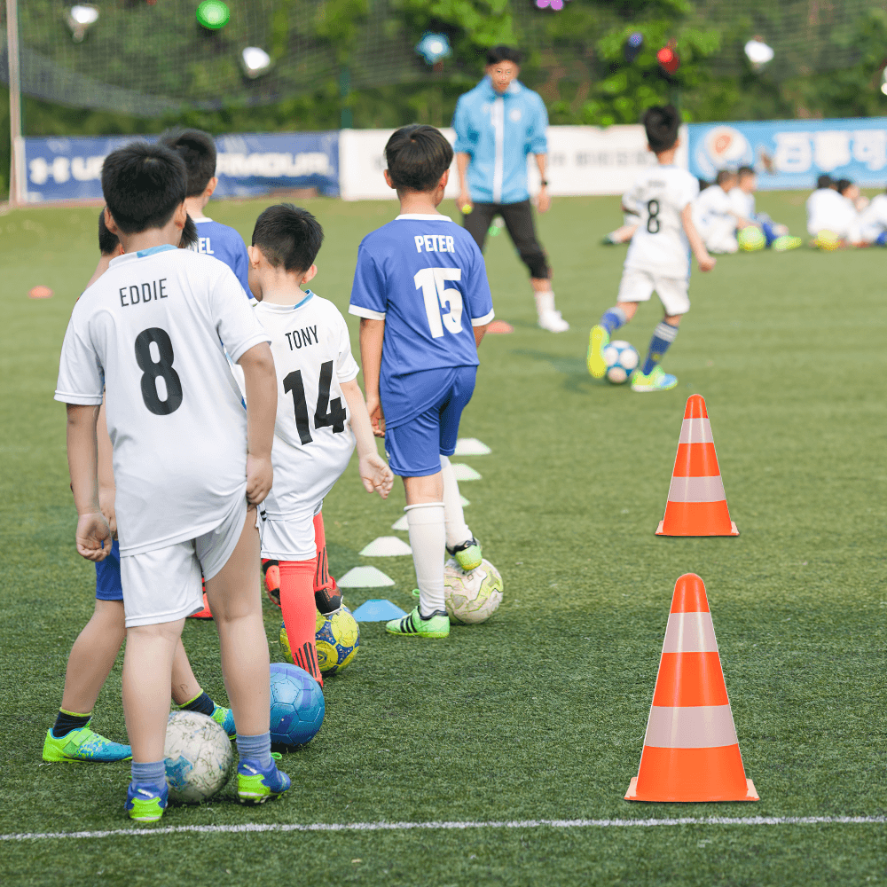 Kids practicing soccer with reflective cones for training on the field. Focus on safety and skill development in football drills.