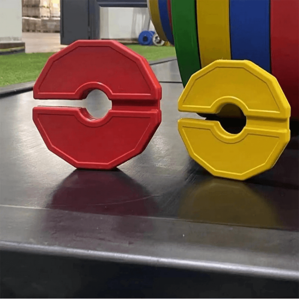 Color-coded rubber weight plates for barbells in red and yellow on gym floor, ideal for precise weight adjustments.