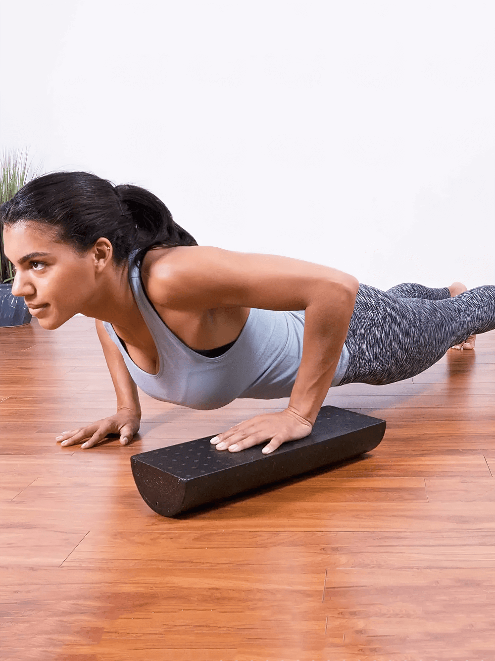 Woman using SF2841 EPP half foam roller for strength training and balance on wooden floor, ideal for Pilates and physical therapy exercises.