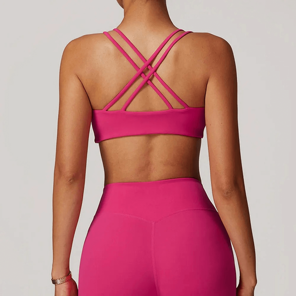 Woman wearing a sexy criss-cross strap sports bra in pink, showcasing high support and breathable fabric perfect for workouts and yoga.