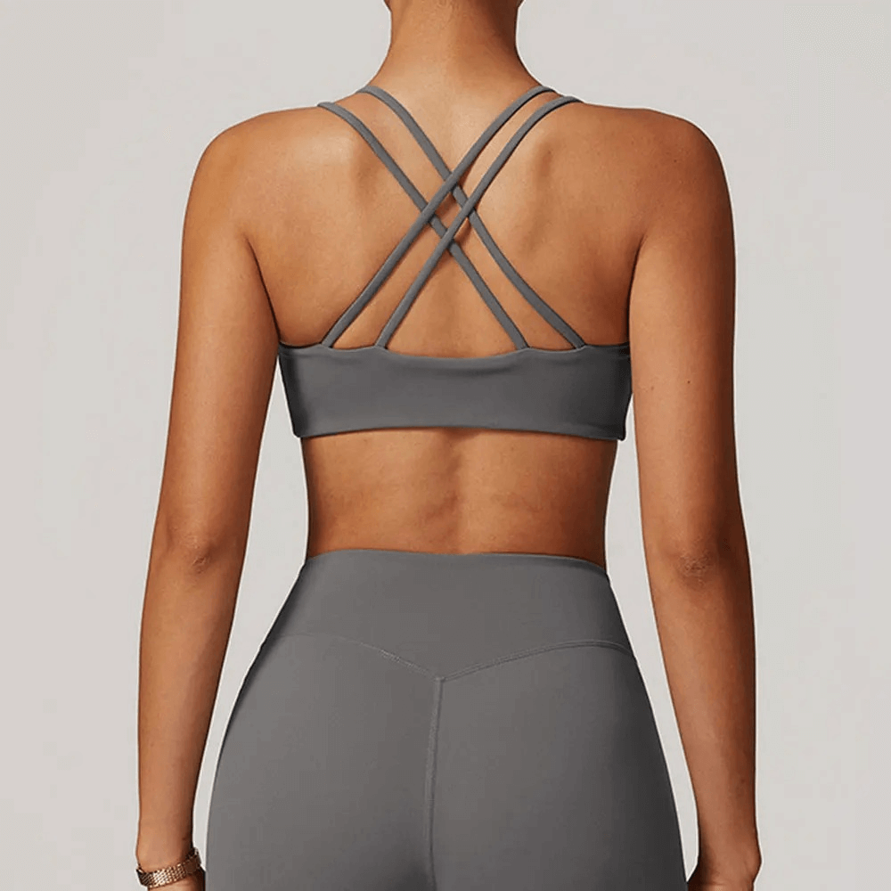 Back view of a woman wearing a sexy criss-cross strap sports bra in gray, designed for high support. Ideal for fitness and workout routines.