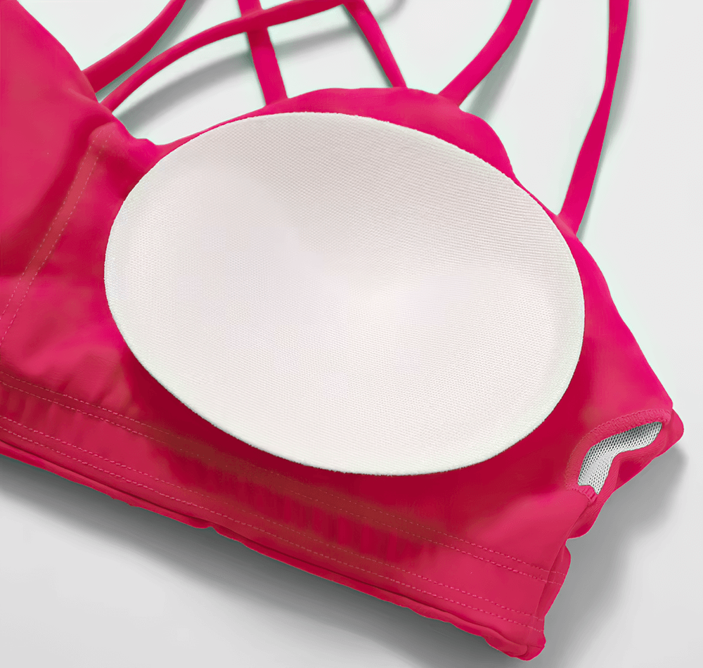 Close-up of a pink sports bra with crisscross straps and a white cup insert, showcasing high support and breathable material.
