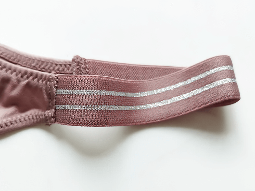 Close-up of pink low-rise G-string panties with silver stripes and durable knit fabric, showcasing stylish detail and sleek design.