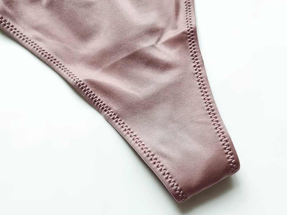 Close-up of a stylish knit low-rise G-string panty in soft pink, showcasing smooth fabric and precise stitching details.