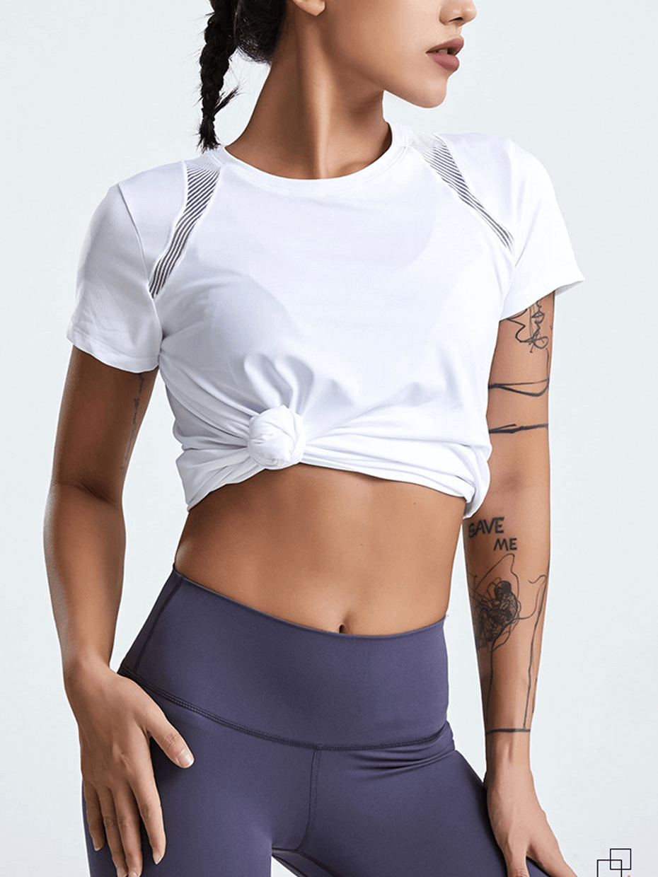 Woman in white short-sleeved running t-shirt with knotted front, paired with purple yoga pants, showcasing fitness and style.