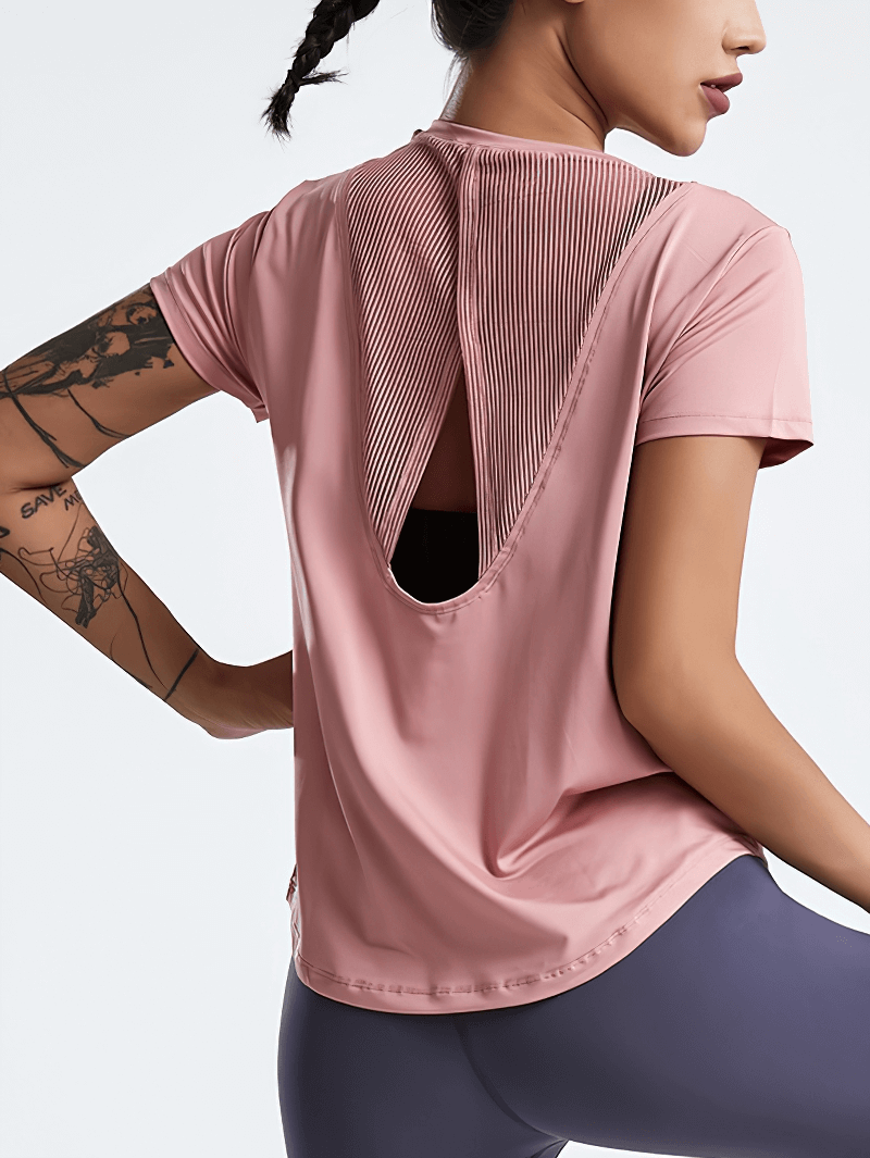Woman wearing pink short-sleeved running t-shirt with hollow back for yoga, highlighting breathable fabric, performance-oriented design.