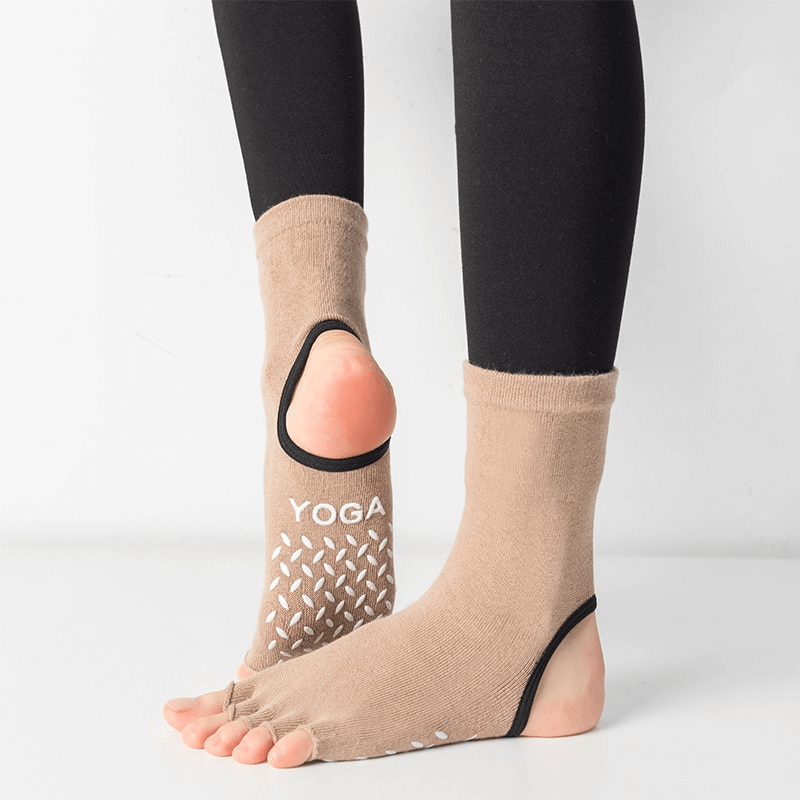 Woman wearing silicone non-slip toeless pilates socks with "YOGA" text, showing grip design on wood floor.