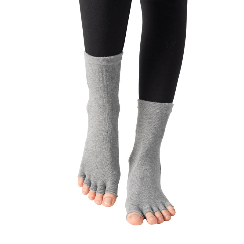 Grey silicone non-slip toeless pilates socks on feet, perfect for yoga and fitness, featuring five-finger design for optimal grip.