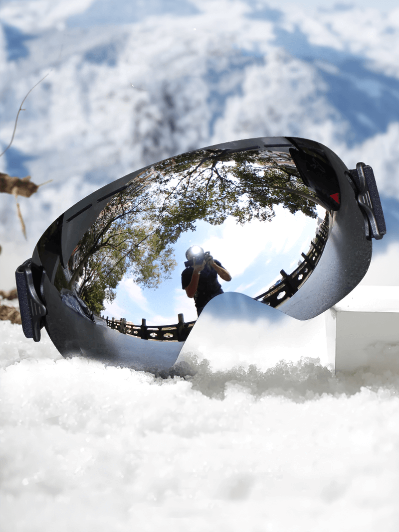Ski goggles with mirror lens reflecting snowy landscape and blue sky, featuring anti-fog UV protection and wide peripheral vision.