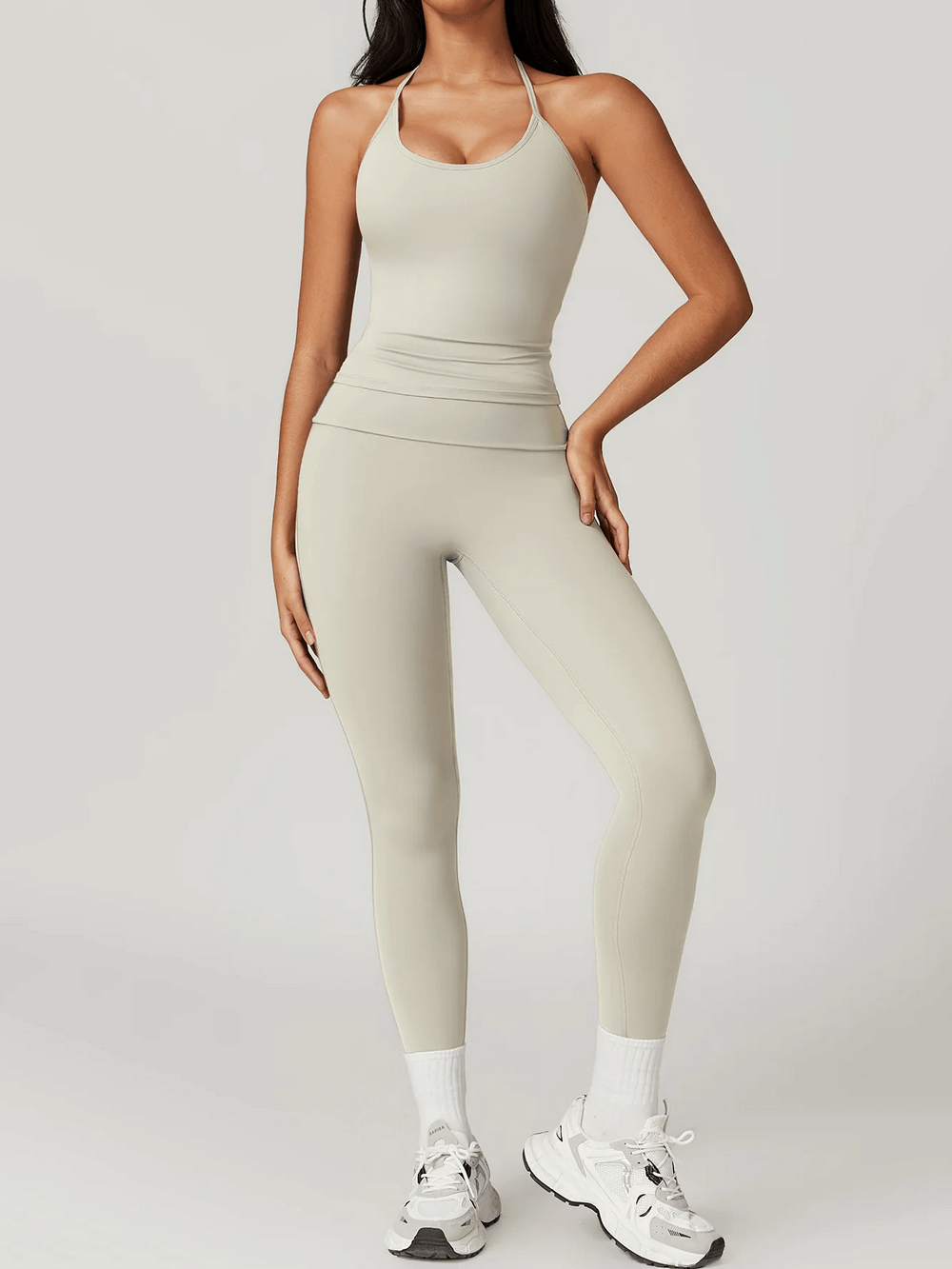 Woman wearing sleek halter neck sports tank for yoga. Ideal for high-intensity training. Durable nylon-spandex blend in stylish beige.