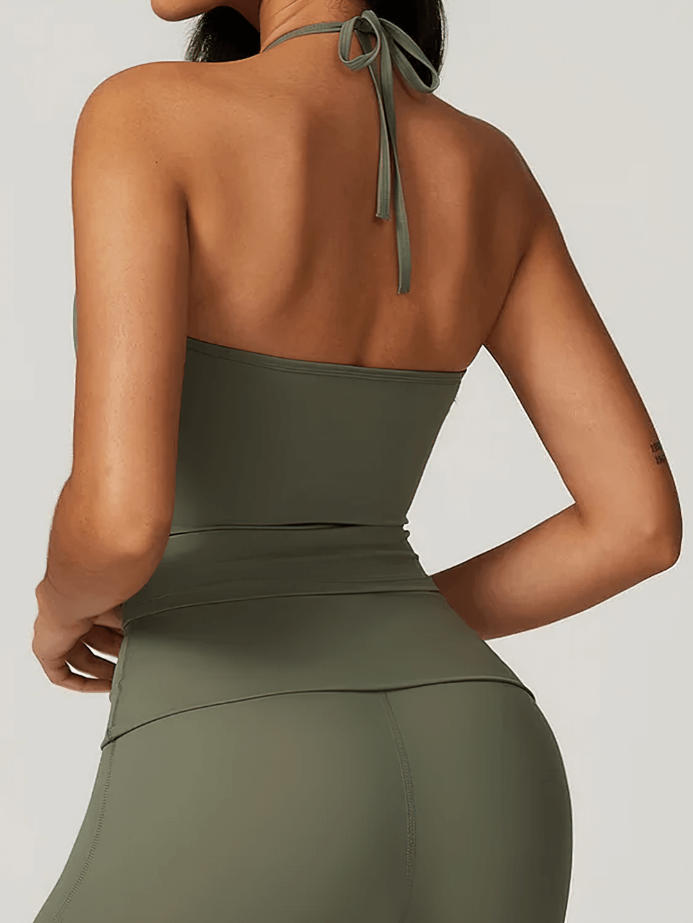 Back view of a woman wearing a sleek halter neck sports tank, ideal for yoga and high-intensity training, in olive green.