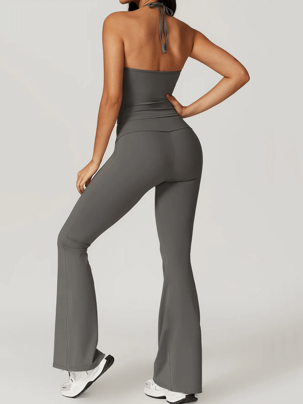 Woman wearing sleek halter neck sports tank and flared yoga pants, showcasing stylish workout attire for high-intensity training.