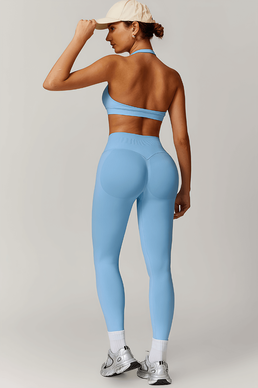 Woman modeling blue sleek sculpt leggings and halter bra activewear set, highlighting back view and seamless, figure-enhancing design.