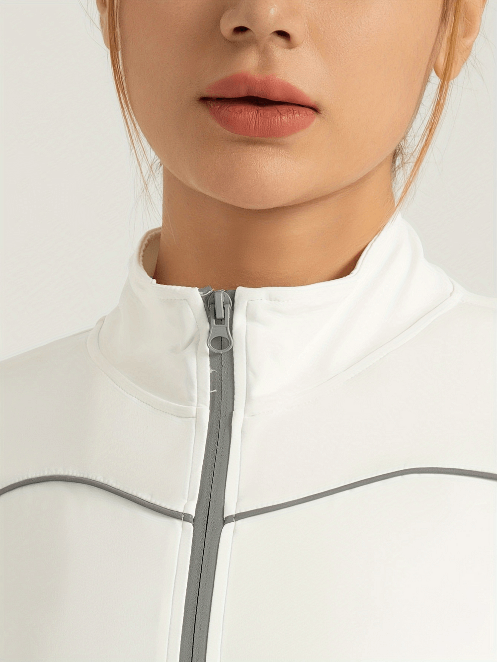 Close-up of white slim fit women's sports jacket with reflective details and full zip closure, featuring thumb holes for secure wear.