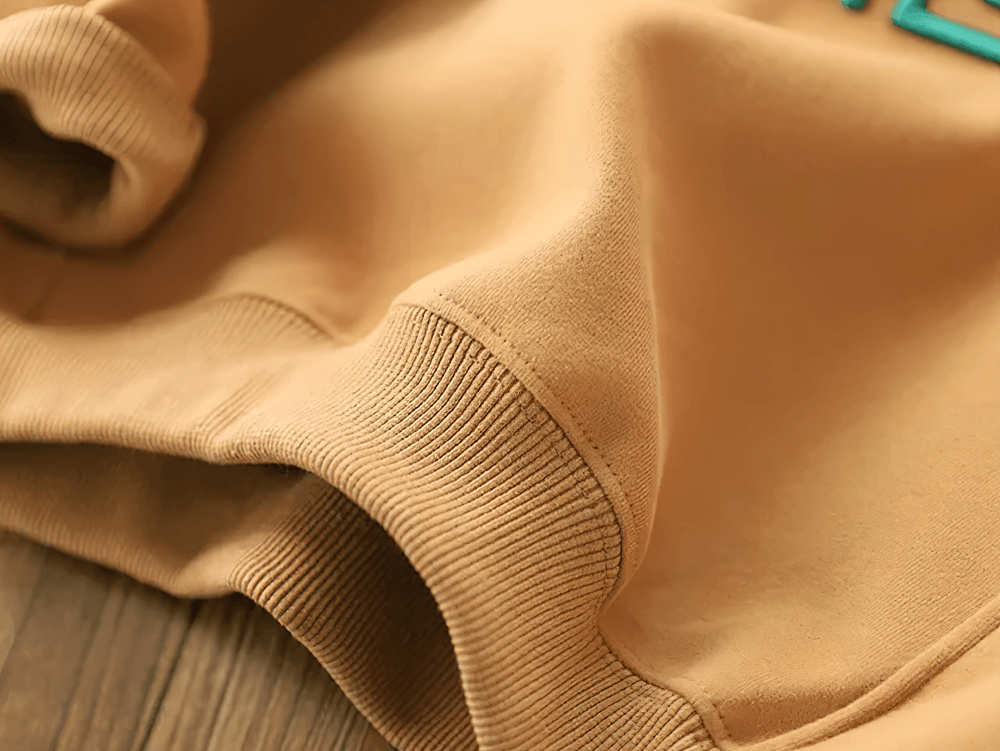 Close-up of soft beige children's sweatshirt with elastic cuff and SMILE graphic detail.