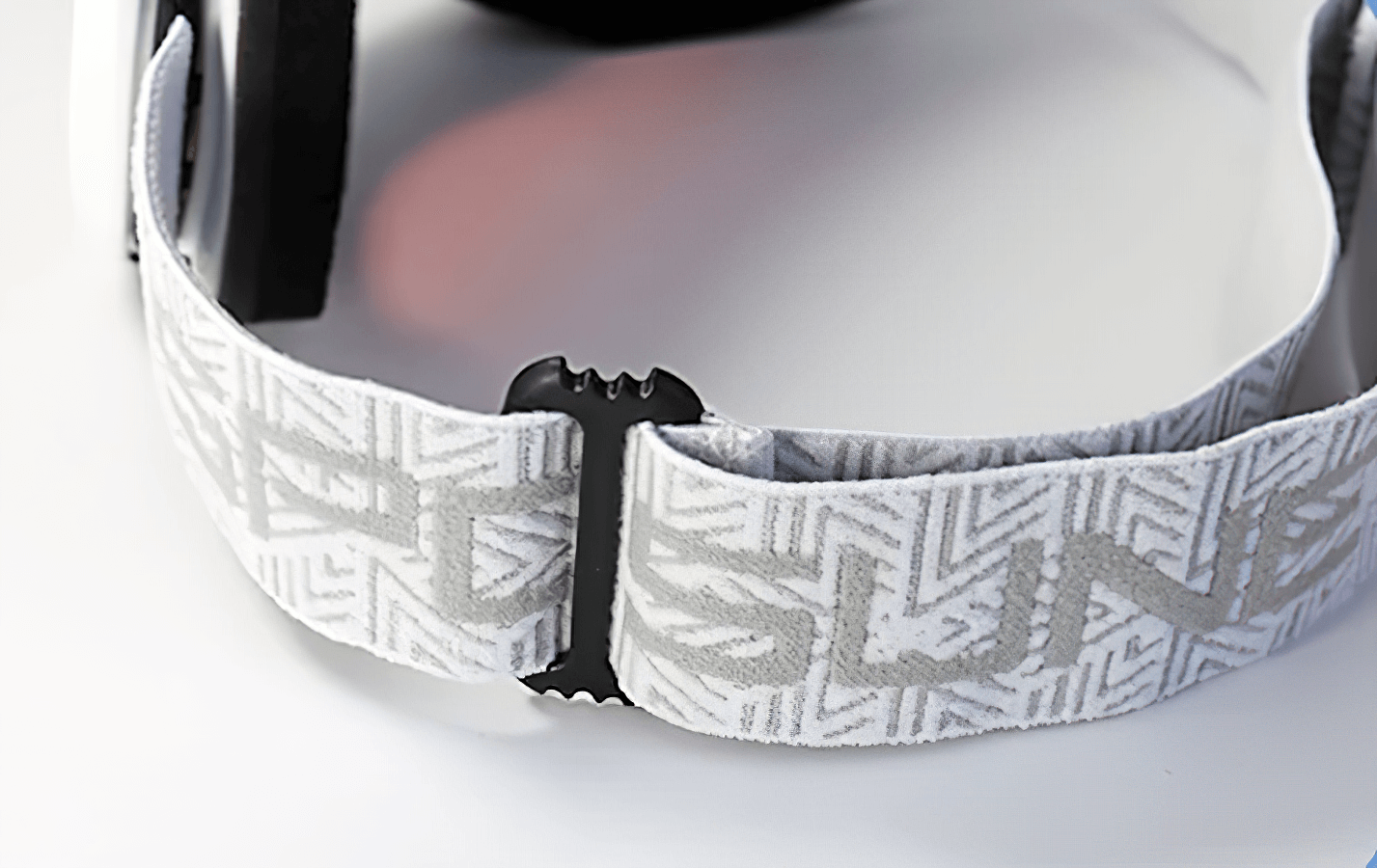 Close-up of snowboarding goggles with geometric-patterned adjustable strap, showcasing sleek black frame and cushioned interior padding.