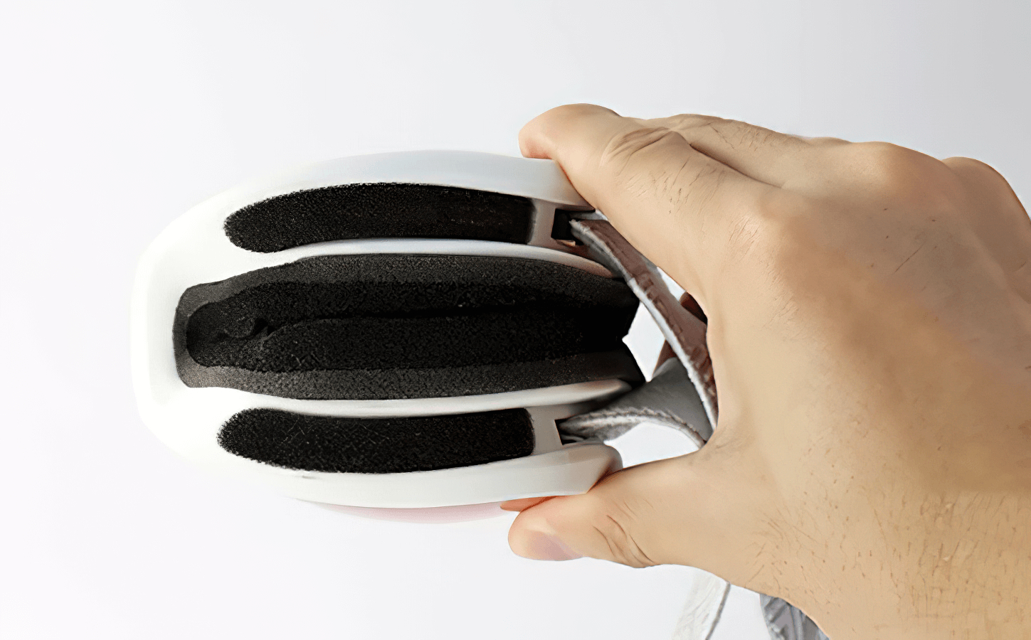 Hand squeezing white bicycle helmet with black padding, showcasing flexibility and comfort.