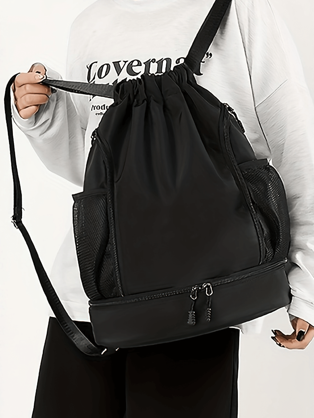 Black spacious nylon backpack with drawstring and zipper, worn by a person in a white shirt.