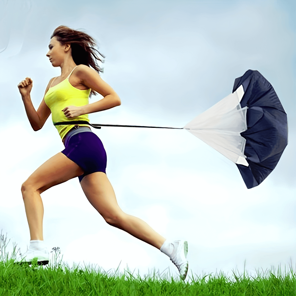 Athlete running with speed training resistance parachute for strength and endurance in a grassy field.