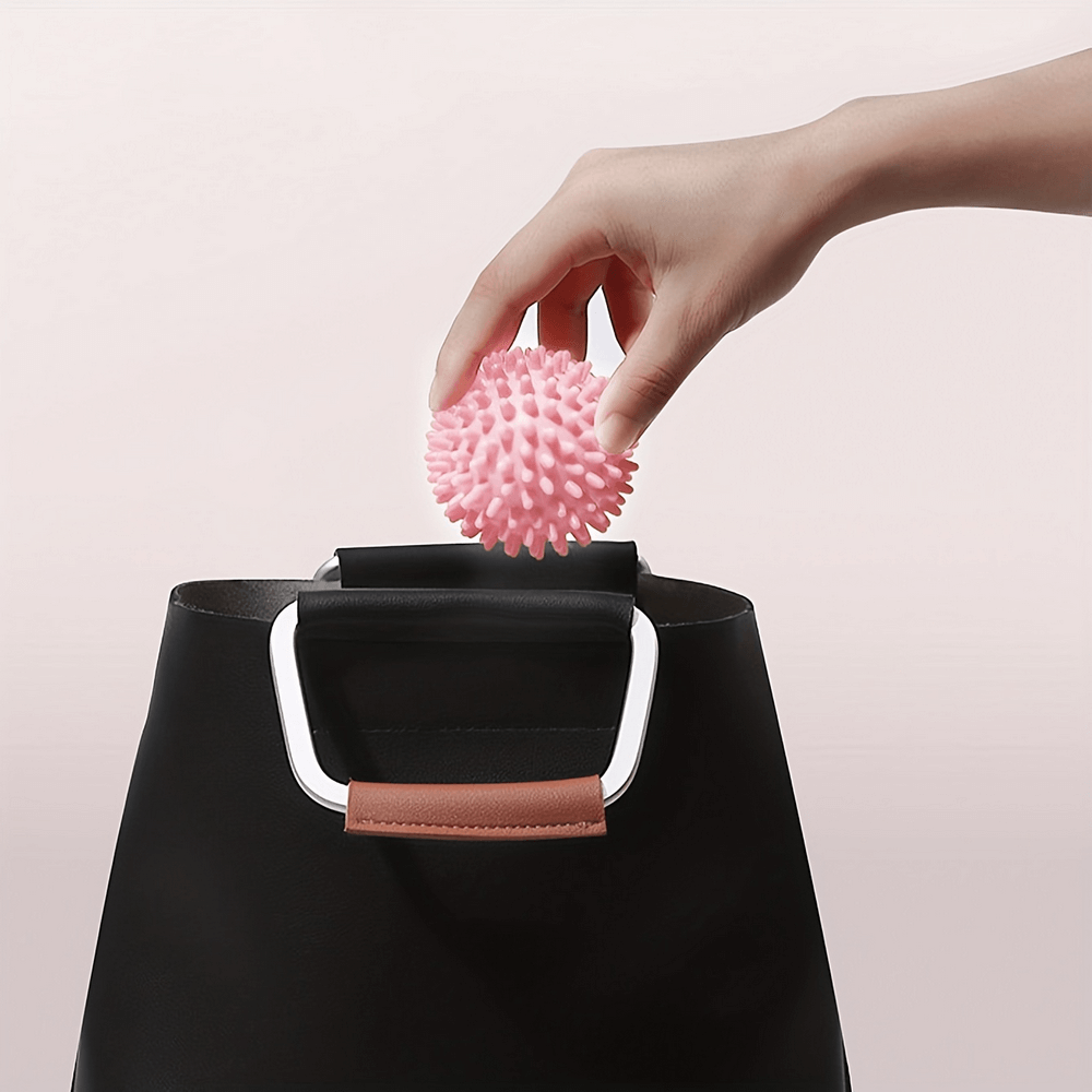 Hand placing a pink spiky massage ball into a black handbag, perfect for portable muscle relief and relaxation.