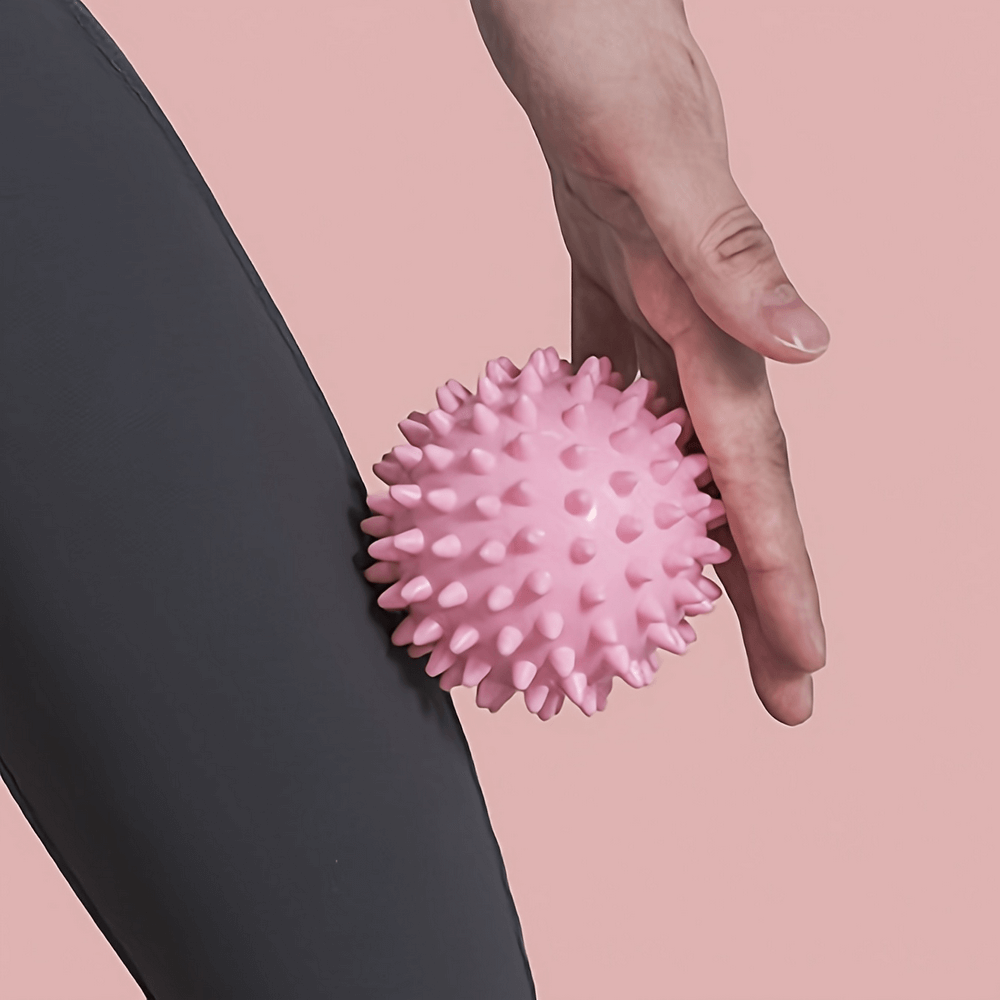 Pink spiky massage ball for deep tissue and muscle relaxation against dark clothing background.