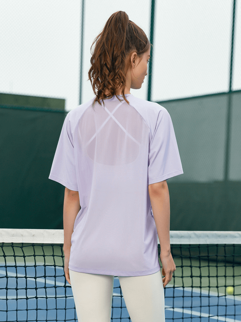 Woman in sports breathable mesh loose T-shirt, quick-dry fabric for yoga, standing by tennis court. Stylish and comfortable activewear.