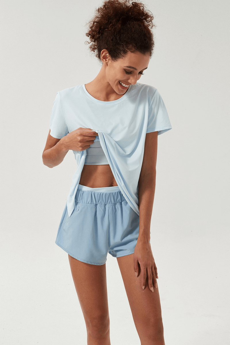 Woman wearing a light blue breathable t-shirt with a back slit, ideal for sports and fitness, paired with matching shorts.