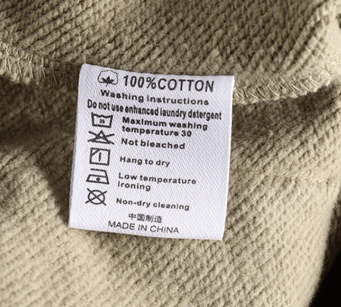 Close-up of a beige 100% cotton clothing tag with washing instructions in English and Chinese.