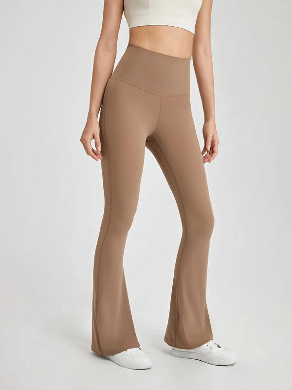 Sporty woman in high-waist flare pants ideal for yoga and fitness, showcasing stretchy fabric. Model in full-length beige athletic wear.