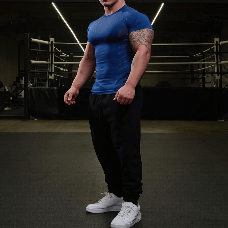 Man wearing blue quick dry workout t-shirt and black pants in gym, showcasing athletic fit and comfort for active lifestyle.