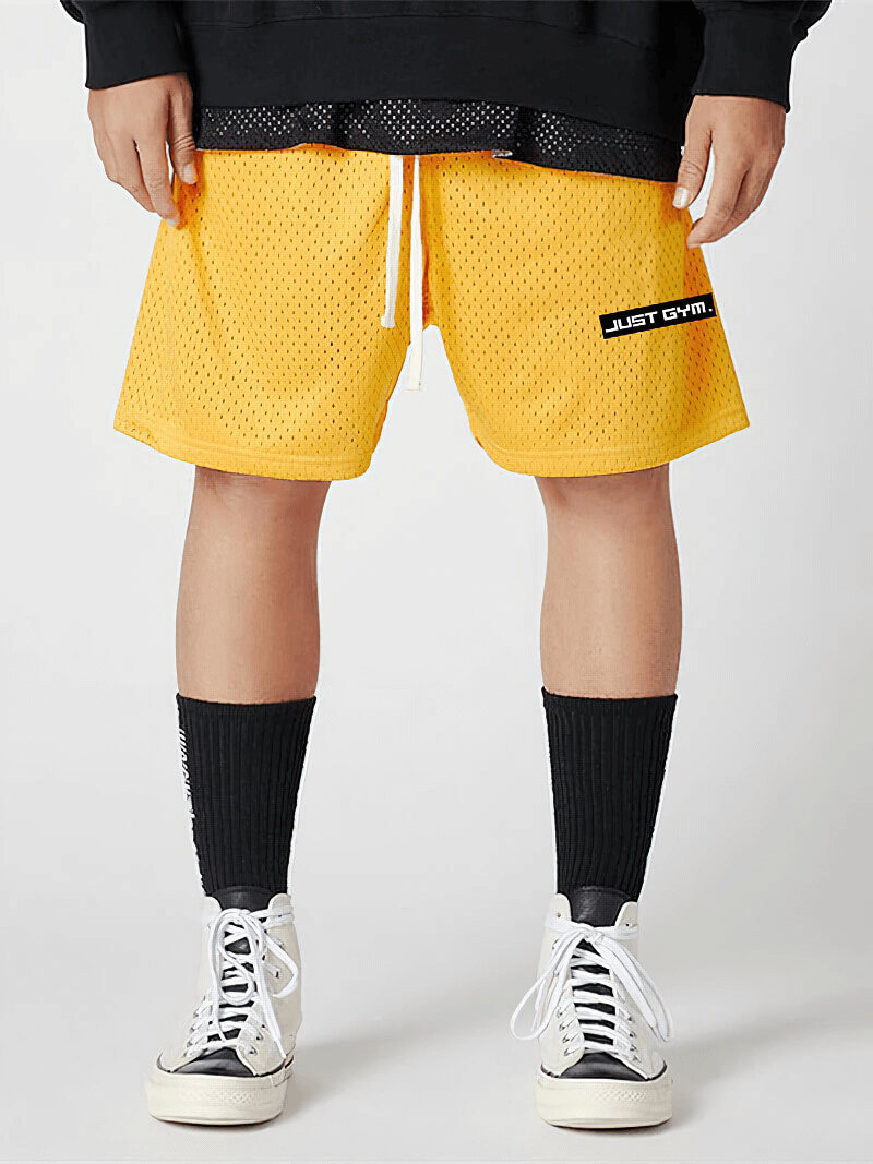 Man wearing yellow sports mesh short shorts with pockets paired with black socks and white sneakers, perfect for athletic activities.