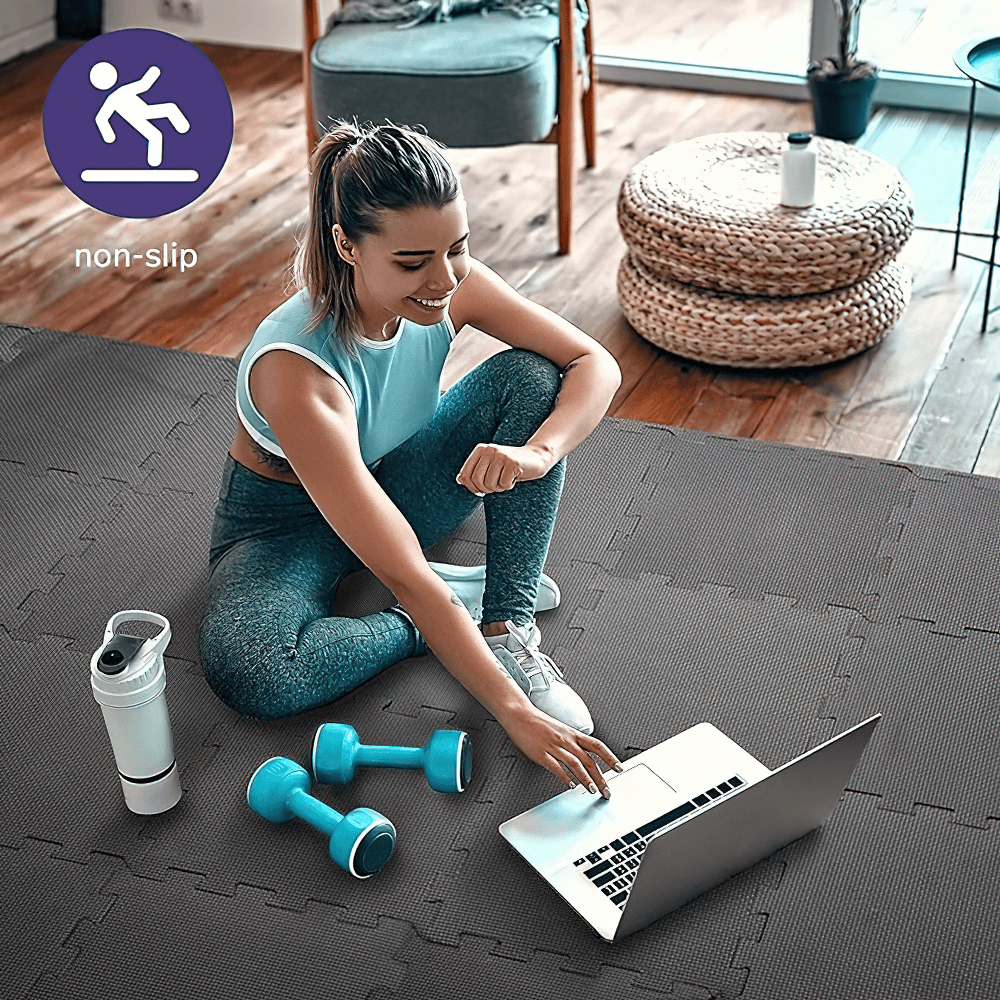 Woman on non-slip gym mat using laptop with dumbbells and water bottle, showcasing stability and protection for workouts and yoga.