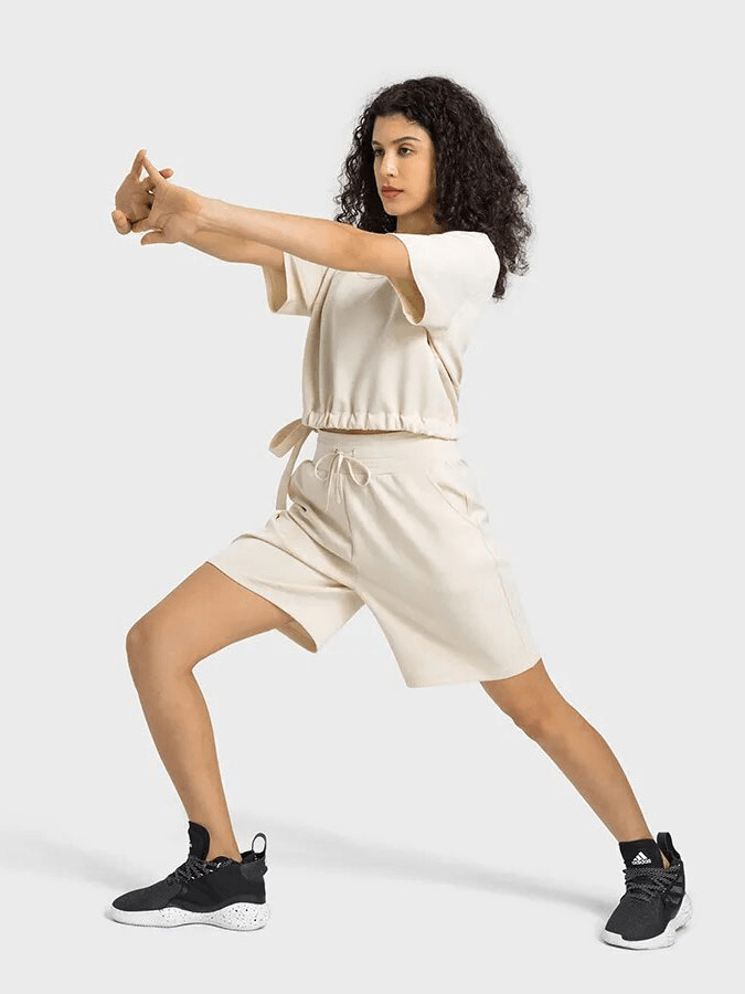Woman in sporty pose wearing white short sleeve crop top and shorts set with adjustable hem, perfect for yoga and fitness.