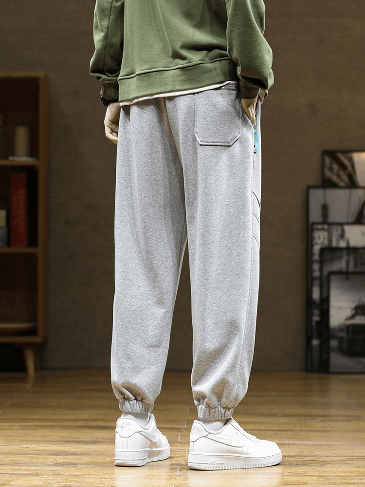 Sporty baggy casual joggers pants for men in gray with side pockets and drawstring, paired with white sneakers.