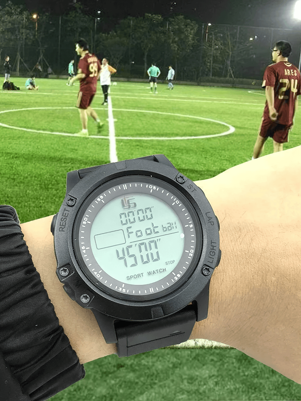 Stopwatch Digital Timer with 100 Lap Memory - SF3468 on wrist, displaying 45:00 minutes, with a football match in the background.