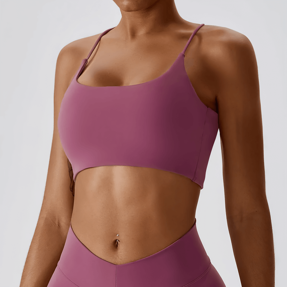 Woman wearing a pink strappy cross-back sports bra with scoop neckline, ideal for gym and yoga, showcasing soft, moisture-wicking fabric.