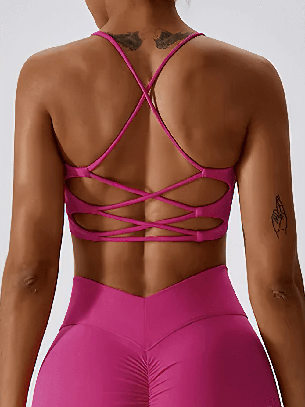 Woman wearing a pink strappy cross-back sports bra, showcasing intricate criss-cross design for activewear style and comfort.