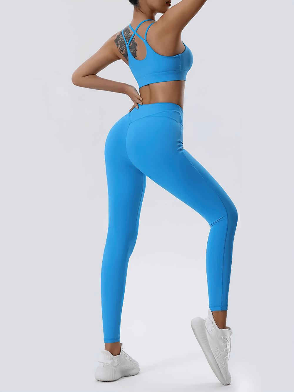 Woman wearing blue strappy sports bra and high-waisted leggings set, perfect for yoga and training. Stylish and breathable activewear.