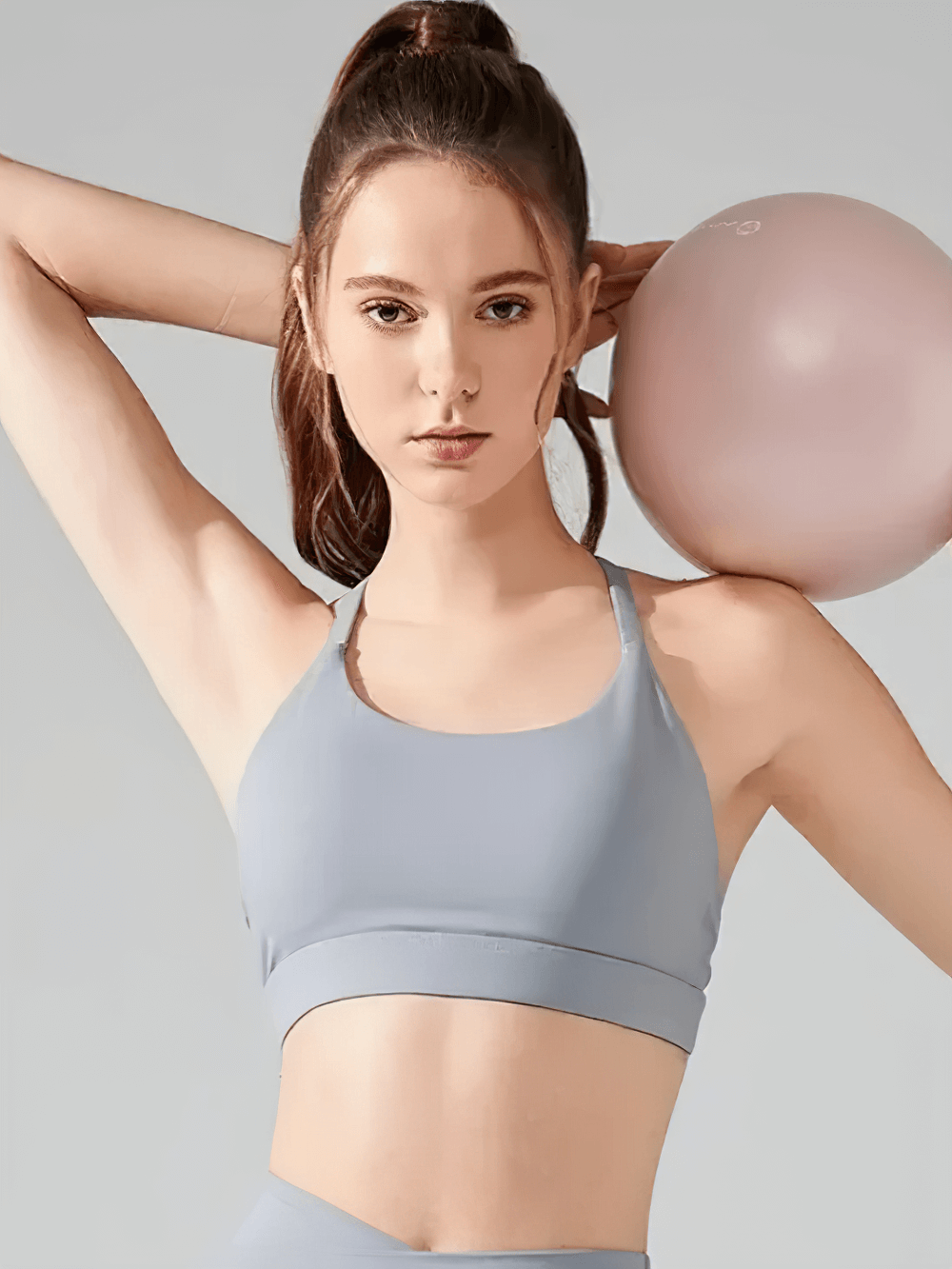 Woman wearing Strappy T-Back Push-Up Sports Bra for Yoga and Gym - SF4033 while holding a yoga ball
