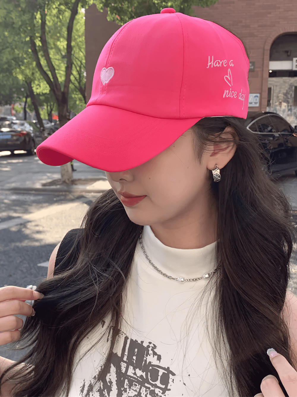 Woman wearing stylish pink baseball cap with stylish lettering, set against a sunny urban backdrop.