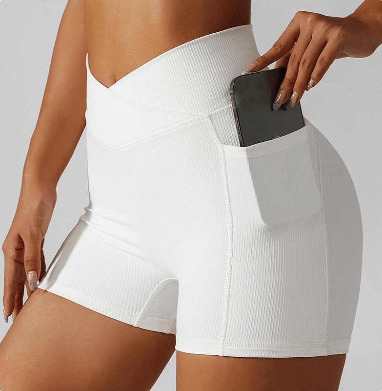 White stylish elastic women's shorts with side pockets, featuring a phone in the pocket, ideal for yoga and activities. Model showcasing fit.