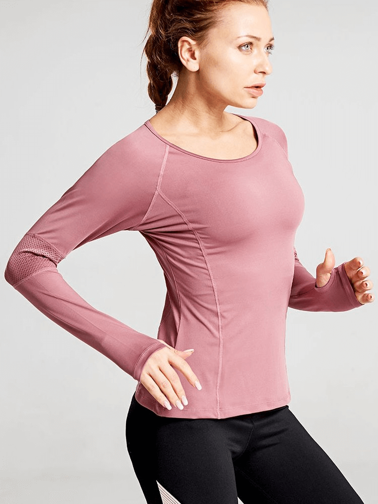 Woman wearing a pink stylish long sleeve yoga top with mesh inserts, demonstrating stretch during exercise.