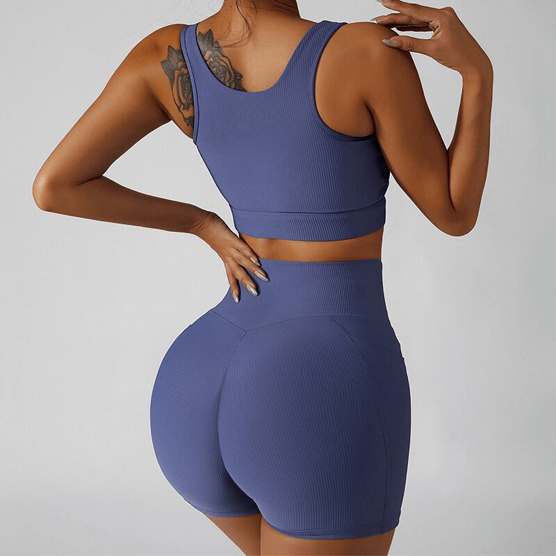 Back view of a model wearing a stylish blue elastic women's sports cropped top and shorts, highlighting eco-friendly and quick-dry features.