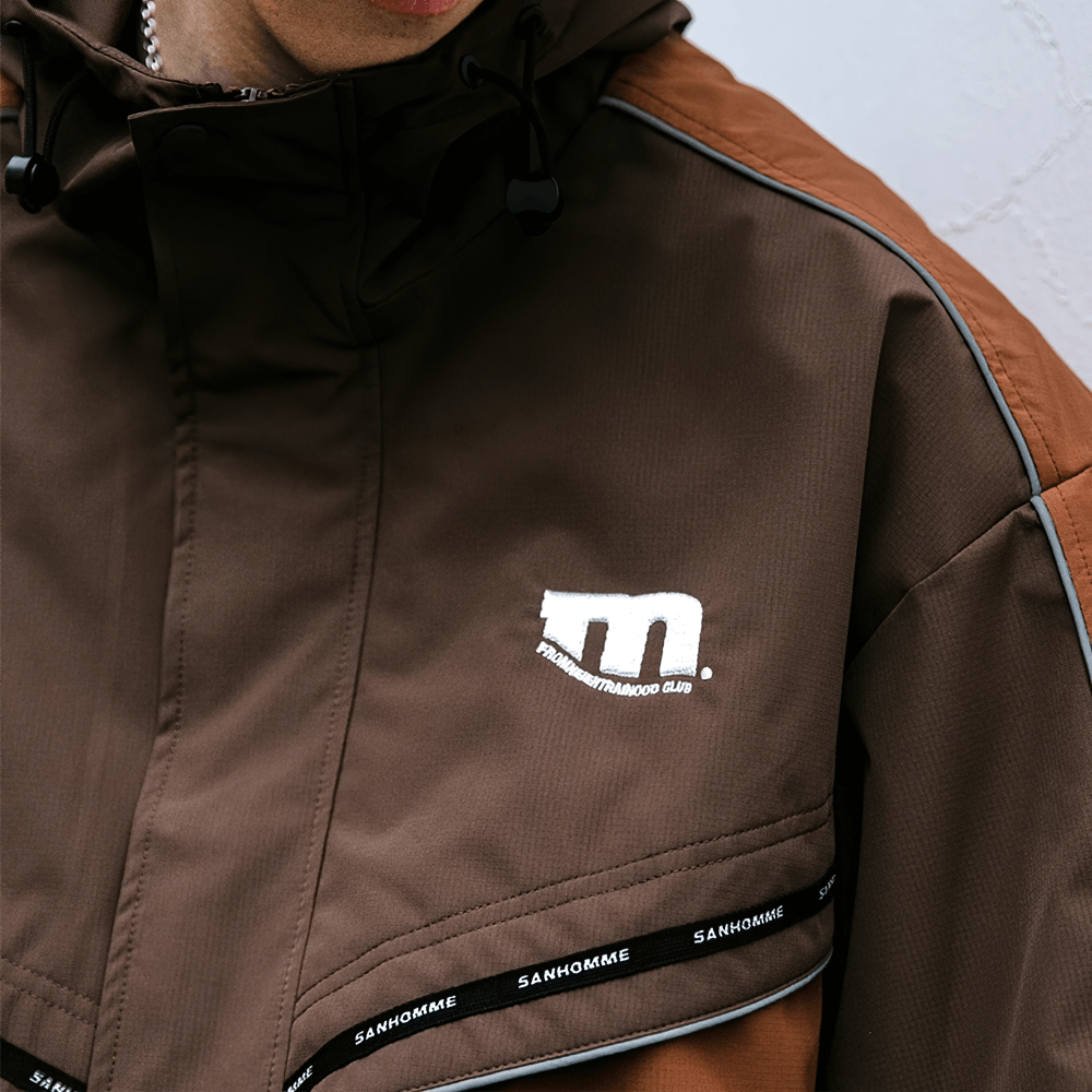 Close-up of a stylish brown patchwork men's outdoor jacket with reflective detailing and hood.