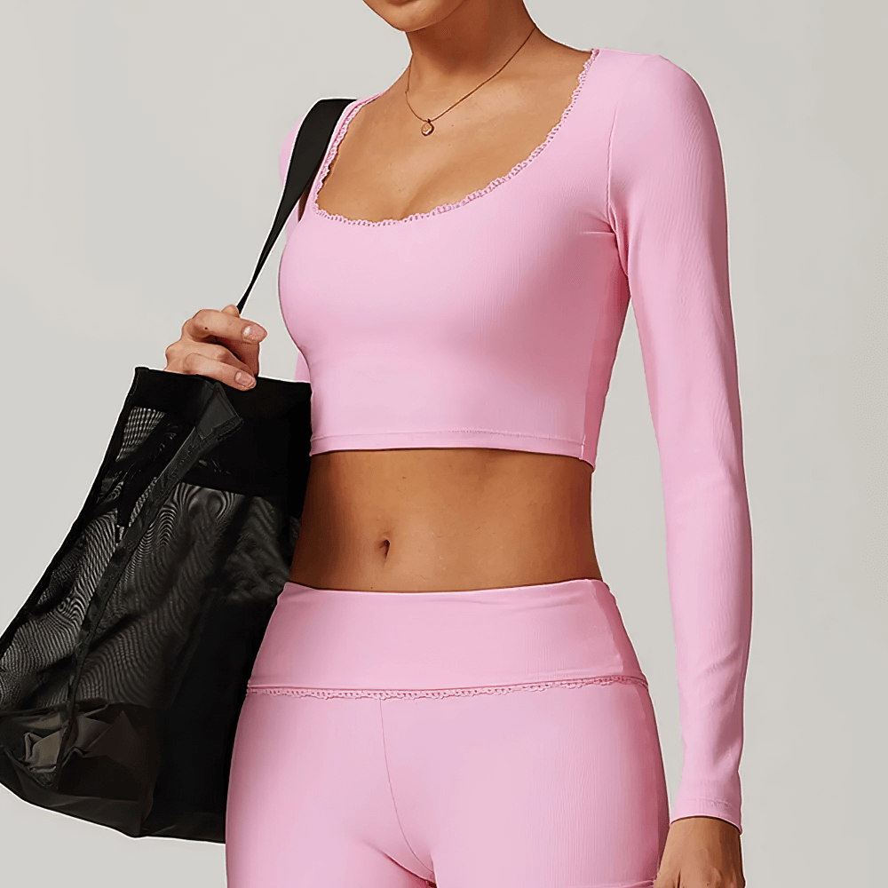 Woman wearing stylish ribbed pink yoga top with long sleeves, holding a black gym bag. Perfect for fitness and outdoor activities.