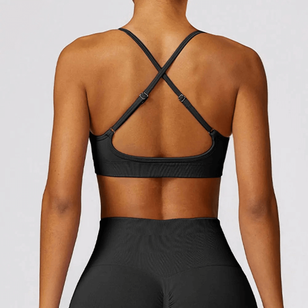 Back view of a stylish seamless yoga bra with criss-cross straps, providing high support for workouts, in black. Model wears matching leggings.