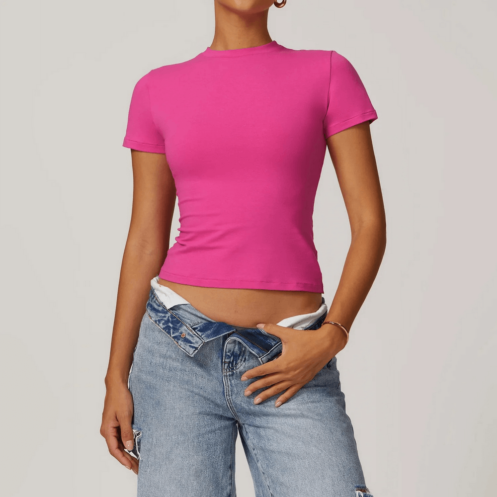 Woman in pink short-sleeve yoga t-shirt and jeans, showcasing stylish athletic wear.