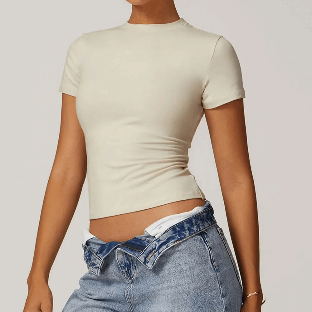 Woman wearing a stylish short-sleeve yoga T-shirt in beige, paired with blue jeans. Ideal for fitness, yoga, and everyday casual wear.