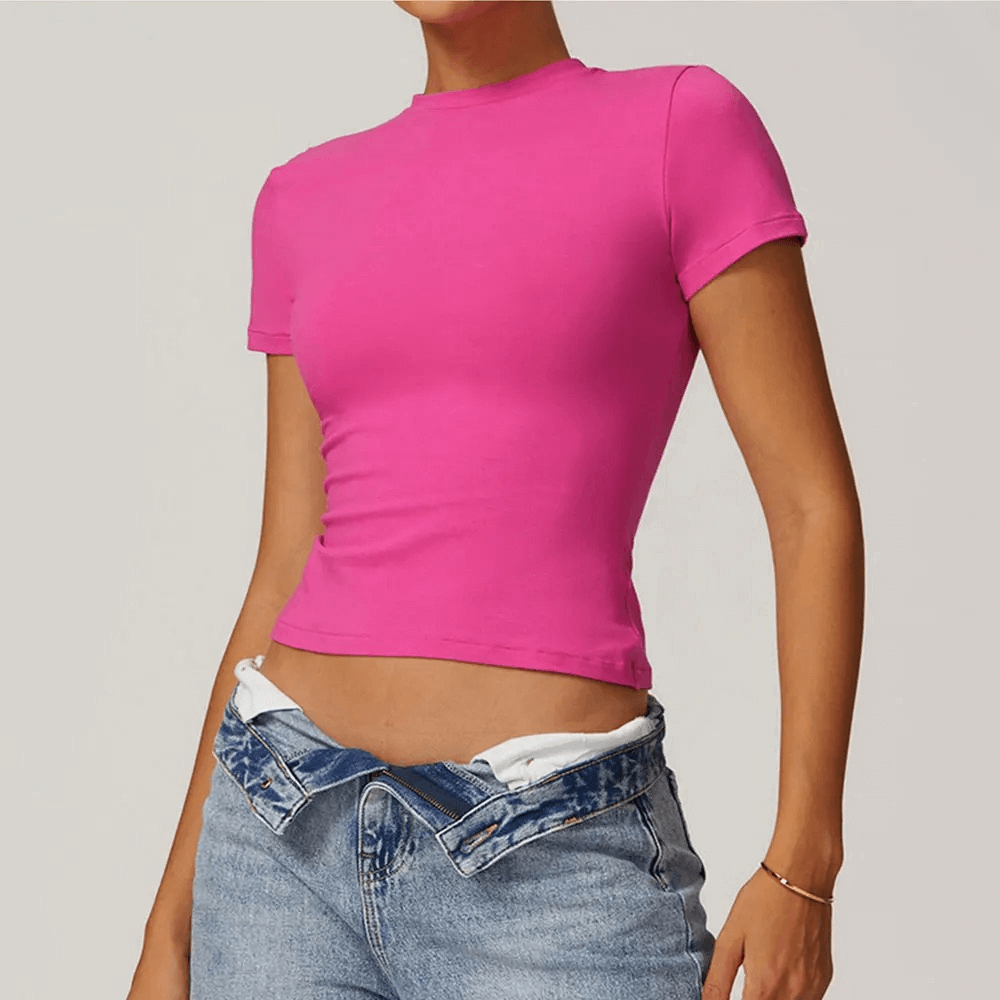 Woman wearing a stylish pink short-sleeve yoga t-shirt paired with jeans, showcasing a trendy and comfortable sport look.